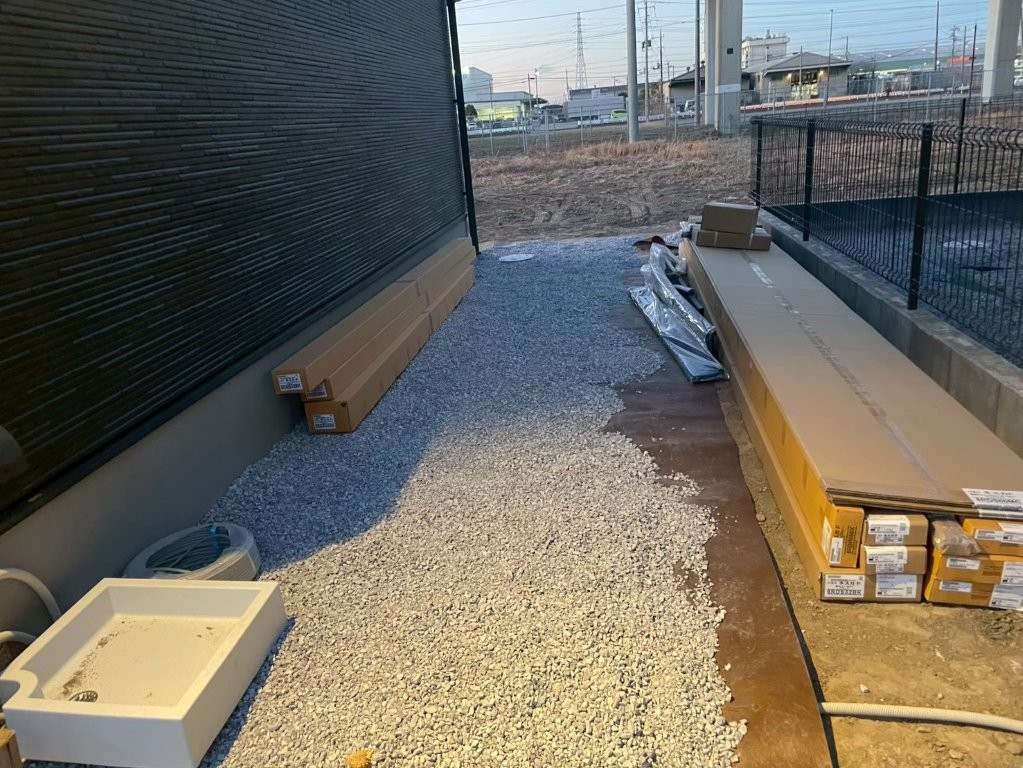 建物脇の犬走りに防草シートと6号砕石を敷き込む施工中の様子。メンテナンス性を高める八潮市O様邸の外構工事