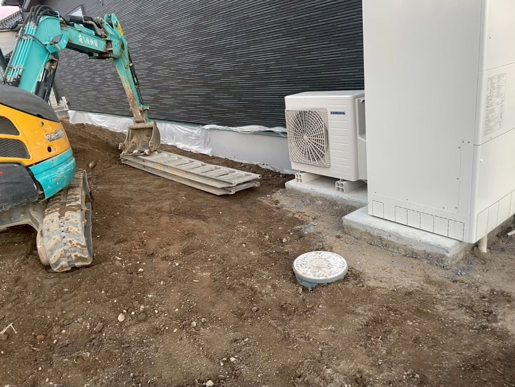 建物脇の設備機器周辺を傷つけないよう養生しながら整地を進める施工中の状況。土間コンクリート前の下地づくり