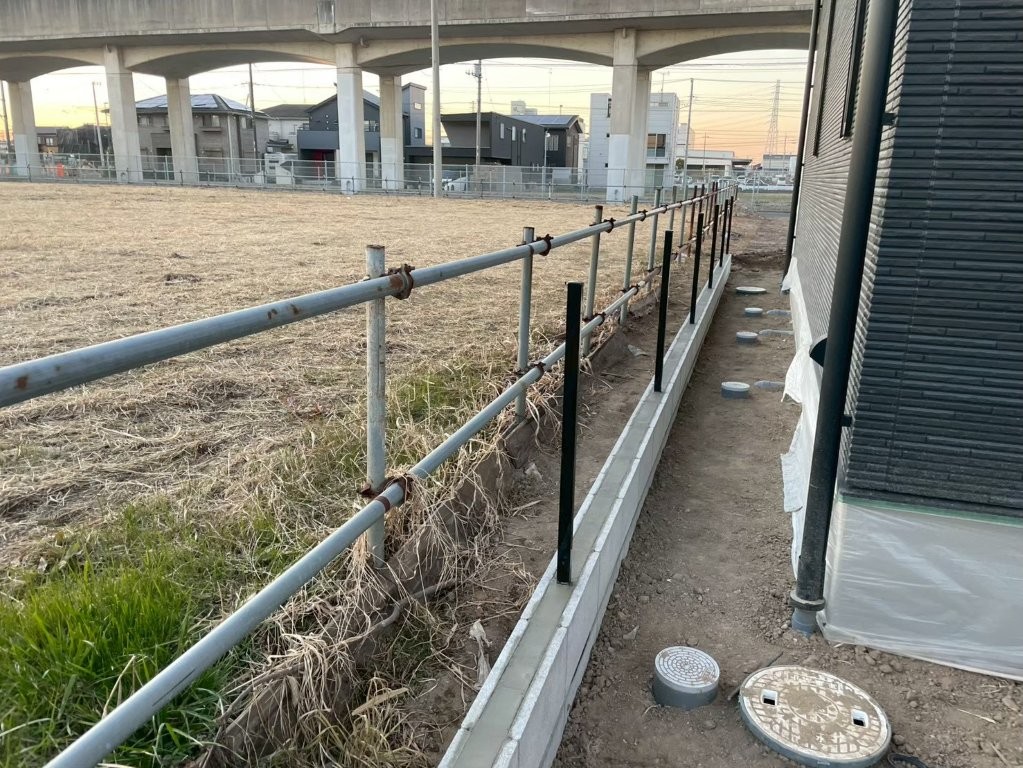 境界ブロック上にメッシュフェンス柱を建て込む工程の様子。外周ラインの直線性を確認しながら進める八潮市の外構工事